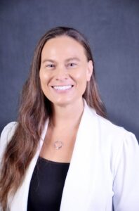 Mary Renouf - podcast host. This is a headshot of a smiling woman with long, brown hair, wearing a silver, circle necklace, a white blazer, and a black top.