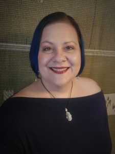 Tressa Gehrke, owner of Blue Lotus Digital Marketing. This is a picture of a smiling Caucasian woman with medium-length hair wearing a navy blue top, wearing earrings and a necklace.